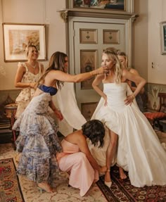 the bride is trying to get her dress put on by three other women in dresses