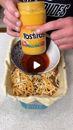 a person pouring sauce into a bowl with shredded cheese on the bottom and other ingredients in it