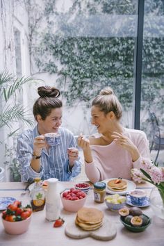 two women sitting at a table with food and drinks