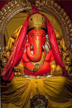 an elephant statue with red cloth draped around it's head and eyes, sitting in front of a gold frame