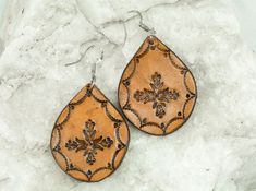 a pair of brown leather earrings sitting on top of a white stone slab covered in snow