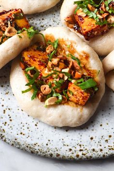 several pita breads on a white plate topped with chopped nuts and green garnish