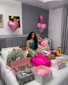 a woman sitting on a bed surrounded by boxes and balloons in the shape of hearts