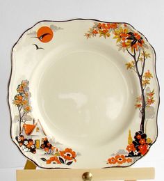 a white plate with an orange and black design on the rim is sitting on a wooden stand