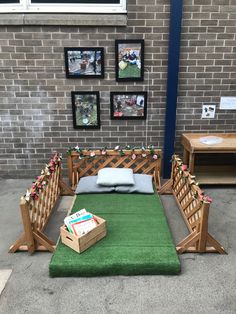 a green area rug and wooden benches in front of a brick wall with pictures on it