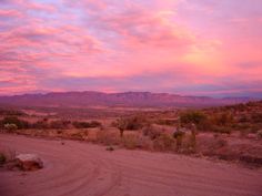 a dirt road in the desert with mountains in the background at sunset or sunrise time