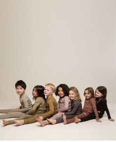 a group of children sitting on the ground in front of a white wall with their legs crossed