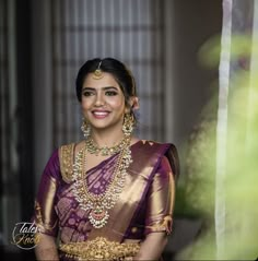 a woman in a purple and gold saree smiles at the camera while posing for a photo