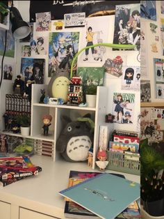 a desk topped with lots of books and toys next to a wall covered in pictures