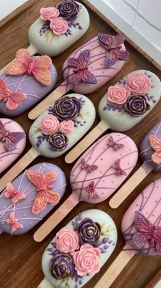 some pink and purple cupcakes are in a box on a wooden tray with toothpicks