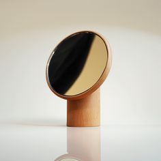 a round mirror sitting on top of a wooden stand next to a white wall and floor