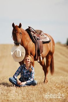 a woman kneeling down next to a brown horse in a field with a hat on it's head