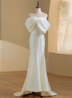 a mannequin is dressed in a white dress on a wooden floor next to a window