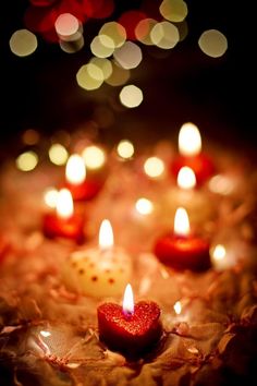 many lit candles are arranged in the shape of a heart on a cloth with some lights behind them