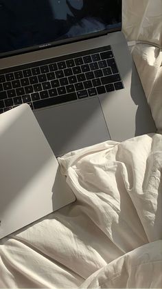 an open laptop computer sitting on top of a white bed covered in sheets and blankets