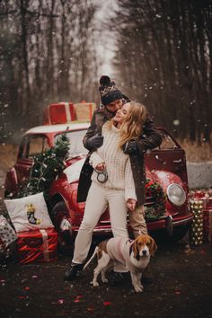 a man and woman standing in front of a red car with christmas presents on it