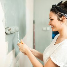 a woman is painting the wall with white paint and she is smiling at the camera