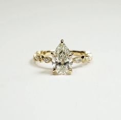 a yellow gold ring with a pear shaped diamond in the center and leaves around it