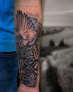 a man's arm with a cross and bird on it, surrounded by roses