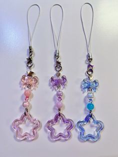 three different colored beads hanging from silver earwires on a white surface with one beaded star and the other shaped like a flower