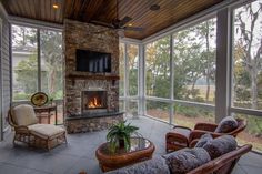 a screened porch with wicker furniture and a stone fireplace in the center surrounded by glass walls