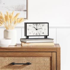 a clock sitting on top of a wooden table next to a vase with dry grass