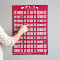 a woman is writing on a red calendar wall hanging on a gray wall and holding a pen in her hand