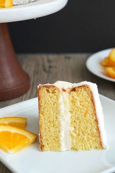 a slice of cake with white frosting on a plate next to orange wedges