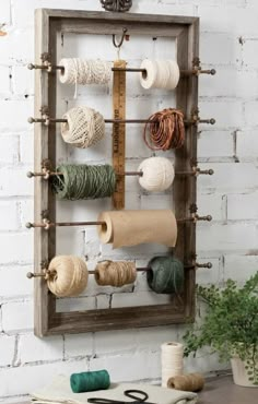 a wooden frame with yarn and scissors hanging on it's side, in front of a white brick wall