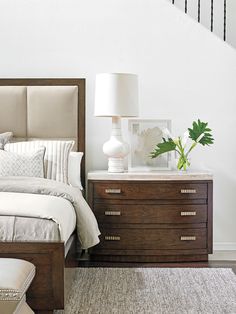 a bed sitting next to a dresser with a lamp on top of it