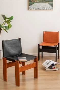 two chairs sitting in a room next to a potted plant and a book on the floor