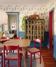 a dining room table with red chairs next to a green cabinet and bookcase in the background