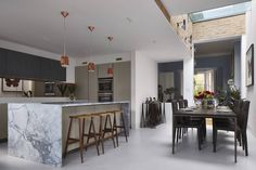 an open kitchen and dining area with marble counter tops, bar stools, and wooden chairs