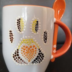 an orange handled spoon sitting on top of a white coffee cup with designs painted on it