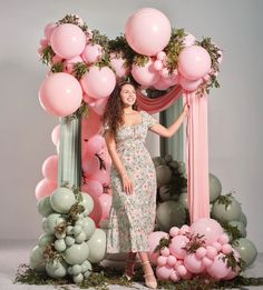 a woman standing in front of a pink and green arch with balloons on the sides