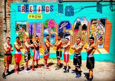 a group of men standing next to each other in front of a wall with graffiti on it