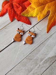 two racoon shaped earrings sitting on top of a wooden floor next to leaves