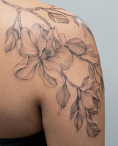 the back of a woman's shoulder with flowers and leaves tattooed on her arm