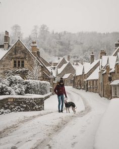 a woman walking her dog on a snowy day in the village with snow covered houses