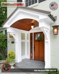 the front entrance to a white house with wood door and arched entryway, surrounded by greenery