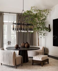 a living room with a round table and chairs in front of a plant hanging from the ceiling