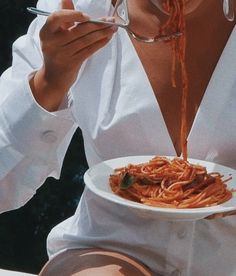 a woman is eating spaghetti from a white plate