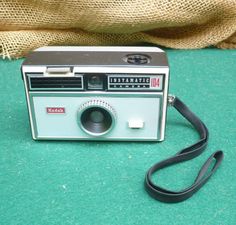 an old fashioned camera sitting on top of a green table next to a burluck bag