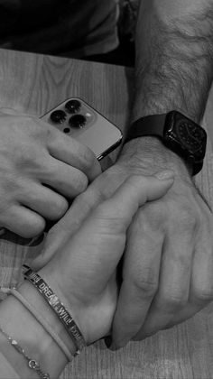 two hands holding each other over a wooden table with bracelets on it's wrist