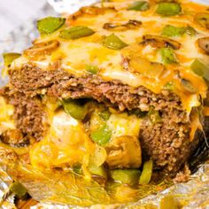 a meatloaf covered in cheese and green peppers on tin foil with a bite taken out