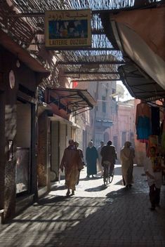 several people walking down an alley way in the middle of town with shops on either side