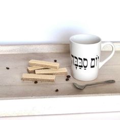 a white coffee cup sitting on top of a wooden table next to some cookies and a spoon