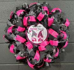 a pink and black mesh wreath on a brick wall with the words sweet as can be