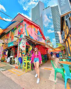 a woman standing in front of a colorful building with lots of chairs and tables around it