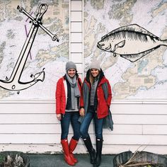 two women standing next to each other in front of a wall with fish on it